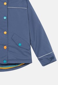 Blaue, wasserfeste Jacke mit bunten Knöpfen (orange, türkis) und einer Seitentasche. Verfügt über Kontrastnähte und ein strukturiertes Innenfutter.