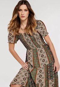 Robe maxi à motifs floraux en vert, orange et blanc. Caractéristiques des manches bouffantes, d'un encolure carrée et d'une taille cintrée avec une jupe fluide.