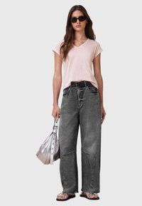 Una maglietta rosa chiaro a scollo a V, jeans larghi grigi, una cintura nera, una borsa a tracolla argentata e infradito neri completano l'outfit informale.