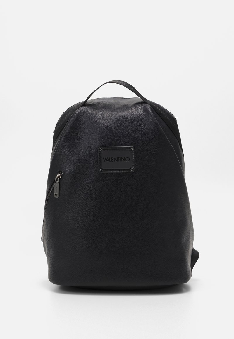 Black leather backpack with a textured surface, rounded shape, and a top handle. Features a front zip pocket and a brand logo plate.