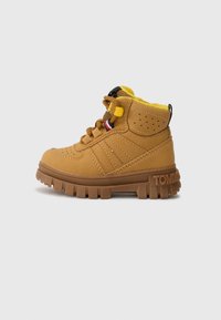 Des bottes chelsea en cuir marron présentent un dessus texturé, une doublure en polaire jaune, des lacets et une semelle en caoutchouc épaisse avec un logo sur le talon.