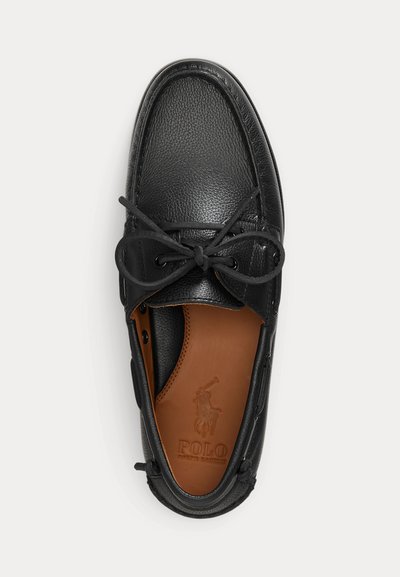 Juodi odiniai laivo batai su batraiščiais, surištais į kaspiną, rudas padas su Polo Ralph Lauren logotipu, matomi iš viršaus ant balto fono.