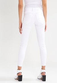 Jeans slim bianchi con vita alta, caratterizzati da un design a cinque tasche e cuciture sottili. Abbinati a sandali con tacco bianchi.