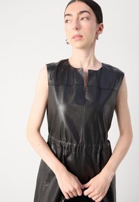 Schwarzes Lederkleid ohne Ärmel mit Rundhalsausschnitt, geraffter Taille und glatter Textur. Verfügt über eine subtile Nahtdetails auf der Vorderseite.