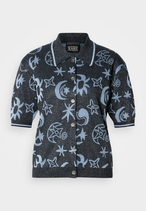 Lyhythihainen neuletakki tummassa kankaassa, joka on glitteröivä ja jossa on sinisiä taivaankappaleita kuvaavia kuvioita. Klassinen kaulus ja napitus.