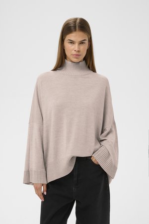 Šviesiai pilkas megztas polo tipo megztinis su laisvu siluetu, raukšlėtėmis ant rankovių ir apatinio krašto. Derinamas su tamsiomis kelnėmis, lygia tekstūra ir kasdiene estetika.