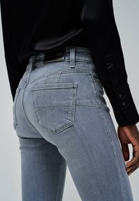 Jeans ajustados grises de denim, con un diseño clásico de cinco bolsillos, detalles de costura sutiles y una etiqueta de cuero negro en la parte posterior de la cintura.