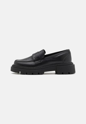 Mocassin en cuir noir avec semelle crantée épaisse et bride avec détail en découpe en forme d'étoile, présenté en profil côté sur fond blanc.