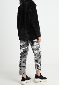 Sort faux fur frakke med spids krave, båret over grå camouflage cargo bukser. Sorte sneakers fuldender outfittet.