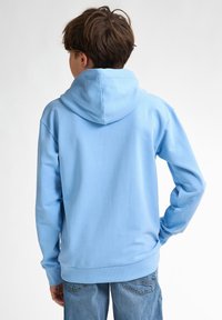 Hanorac bleu deschis cu o glugă mare, mâneci lungi și o croială lejeră. Fabricat dintr-un material moale, dispune de mansete și o margine ribată.