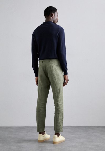 Marineblauwe gebreide langemouwen shirt met kraag, gecombineerd met lichtgroene op maat gemaakte broek en beige sneakers. Minimalistisch ontwerp met een moderne pasvorm.