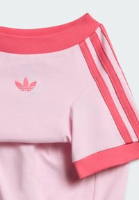 Κοντινή λήψη ανοιχτό ροζ μπλούζας Adidas με κοραλλί ριμπ λαιμόκοψη, μανσέτες στα μανίκια και τρεις λωρίδες στον ώμο, με το λογότυπο Adidas trefoil.