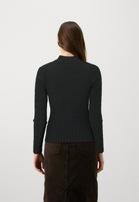 Haut noir à manches longues à côtes avec un col, présentant un design ajusté et un tissu texturé, accompagné d'une jupe marron.