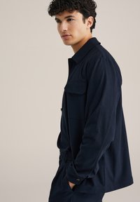 Marineblå jacka i ett mjukt material med rak skärning, utrustad med knappstängning fram, två bröstfickor och synliga sömdetaljer.