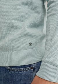 Svijetloplavi pleteni džemper s teksturiranim materijalom, rebrastim manžetama i porubom te malim srebrnim logotipom na donjem lijevom dijelu.