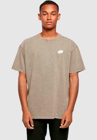 Brun oversized t-skjorte laget av bomull, med rund halsutringning og korte ermer, med en hvit ballonggrafikk på venstre brystområde.