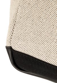 Beige og sort tekstureret taske med en vævet stofkrop, glatte sorte læderdetaljer og en rundet bundkant.