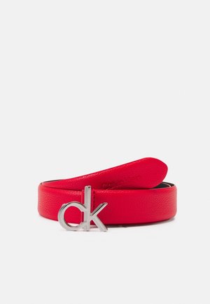 Czerwony skórzany pasek zwinięty, z klamrą z metalowym srebrnym logo "ck" Calvin Klein na białym tle.