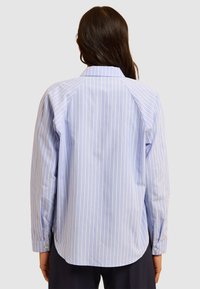 Camicia a righe azzurro chiaro con colletto button-down, caratterizzata da maniche lunghe, vestibilità rilassata e orlo curvo. Tessuto a coste.