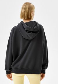 Czarna, oversize'owa bluza z kapturem, z przednią kieszenią typu kangur i dużym kapturem. Posiada ściągacze na mankietach i w pasie, wykonana z miękkiej mieszanki bawełny.