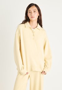 Απαλό κίτρινο, oversized πόλο φούτερ με γιακά και τρία κουμπιά. Μαλακή υφή, μακριά μανίκια με ριχτές άκρες.