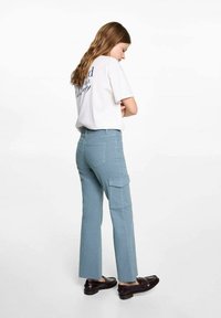 Svetlomodré cargo nohavice s rozšírenými nohavicami, bočnými vreckami a vyblednutou textúrou, v kombinácii s voľným bielym tričkom. Nosené sú hnedé topánky.