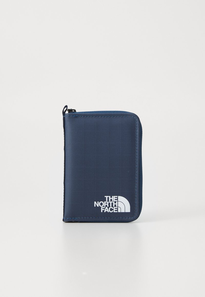 Portefeuille zippé compact de couleur bleu marine avec un motif à carreaux et le logo blanc "The North Face" sur un fond uni clair.