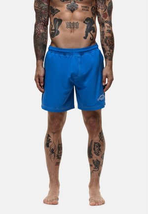 Shorts de bain bleus avec une taille élastique, fabriqués en tissu lisse. Présentent des coutures contrastées et un petit logo sur le bas de la jambe.