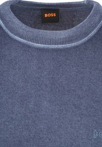 Blauer Strickpullover mit rundem Ausschnitt, glatter Textur und gerippten Abschlüssen. Das Markenlabel "BOSS" ist am Kragen angenäht.