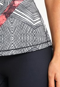Zwart-witte fitness top met geometrisch patroon en roze accenten, slim fit ontwerp en een gladde, lichtgewicht stof. Stiknaaddetails zichtbaar.