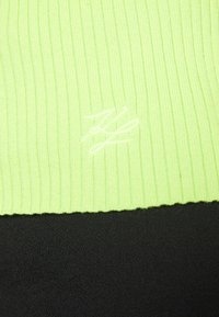 Ribbat ljusgrön tyg med vita broderade initialer ovanför en slät svart tygbakgrund.