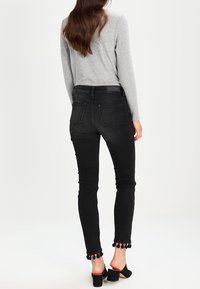 Jeans negros ajustados con cintura alta, con un tejido texturizado y adornos de borlas en el dobladillo. Combinados con un suéter gris de canalé ajustado.