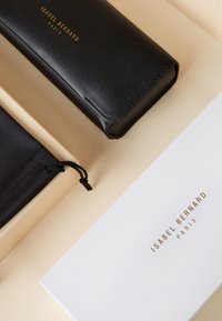 Zwarte leren hoes met een gladde textuur en goudfolie branding aan de voorkant, vergezeld van een zwarte stoffen zak en een witte kaart.