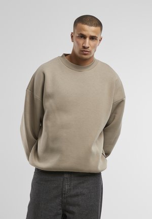 Beige oversized sweatshirt with a crew neckline, wide sleeves, and soft texture. Paired with dark gray denim pants.