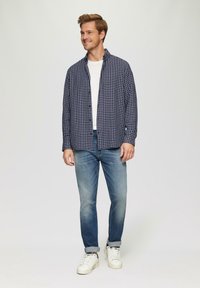 Marineblauwe geruite shirt over een witte ronde hals, gecombineerd met lichtblauwe spijkerbroek en witte sneakers. Casual pasvorm met knoopmanchetten en opgerolde mouwen.