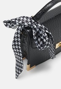 Sac à main en cuir noir texturé avec des accents dorés aux coins et un foulard à motif pied-de-poule noir et blanc attaché à la poignée.