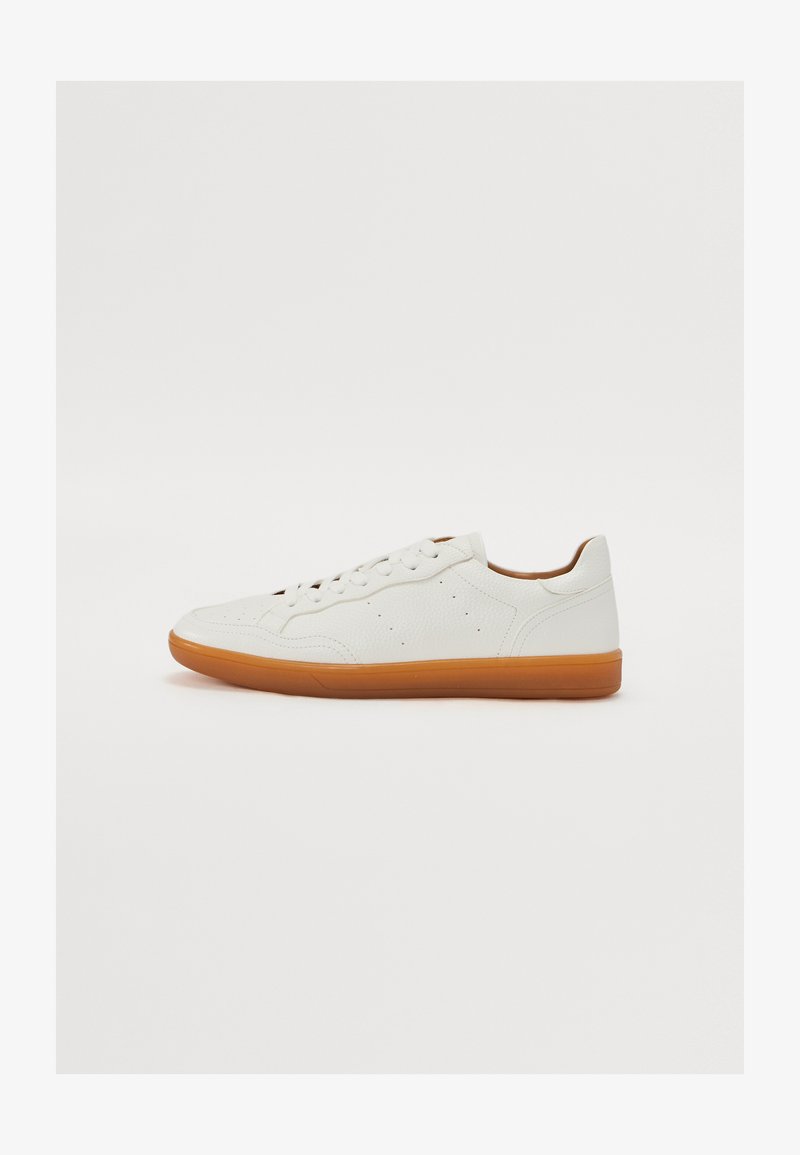 Valge nahkne spordijalanõud, millel on sile tekstuur, ümar nina, kuus auku ja pruun kummitald. Küljel on perforatsioonidega aktsendid.