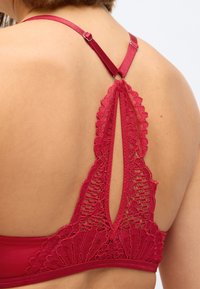 Röd spets- och tyg-bh med en scalloped design på baksidan, justerbara axelremmar och ett nyckelhålskutt.