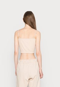 Bežový žebrovaný crop top s tenkými nastavovacími ramínky, se rovnými výstřihem a přiléhavým střihem. Stylizováno s odpovídajícími volnými kalhotami.