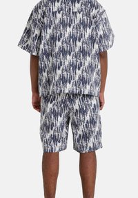 Set van een kortemouwen shirt en shorts in marineblauw en wit, met een gestructureerd patroon van verticale strepen. De stof lijkt lichtgewicht en casual.