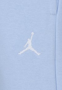 Svetlomodrá bavlnená tkanina má biele vyšívané logo Jumpman, znázorňujúce hráča vo vzduchu s loptou, na textúrovanom pozadí.