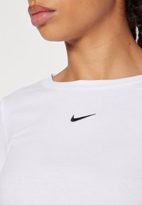 Haut à manches courtes côtelé blanc avec un petit logo Nike noir sur la poitrine. Le tissu semble doux et léger, avec un col rond.
