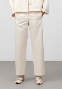Pantaloni color crema in design a gamba dritta, realizzati in un tessuto liscio con tasche laterali. Abbinati a sneakers beige e marroni.