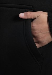 Zwarte sweatstof benadrukt met een hand in de zak. De zak heeft een gebogen opening en toont zacht, gestructureerd materiaal.