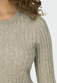 Pull en tricot gris clair avec un motif en torsades, col côtelé et manches ajustées, fabriqué dans un matériau doux avec une finition texturée.