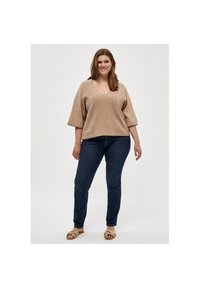 Beige V-Ausschnitt-Pullover aus weichem Strickstoff mit kurzen Ärmeln, kombiniert mit dunkelblauen Skinny-Jeans und hellen Sandalen.