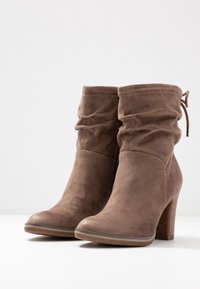Stivaletti in suede marrone con un design arricciato, punta tonda e tacco a blocco. Dettaglio con lacci regolabili sul retro.