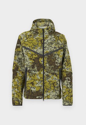 Floral-patterned jacket in green and brown. Features a zip front, hood, and side zip pockets. Lightweight, textured fabric with contrast accents.