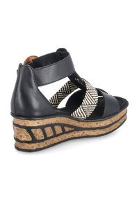 Sandale compensée noire avec une semelle en liège, un design à bandes croisées avec des accents en textile noir et blanc, et une bride arrière robuste.