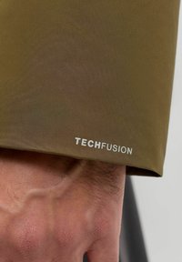 Olivgrüner Stoff mit einem Ärmel mit glatter Textur. Ein weißes "TECHFUSION"-Logo ist entlang der Manschette aufgedruckt.